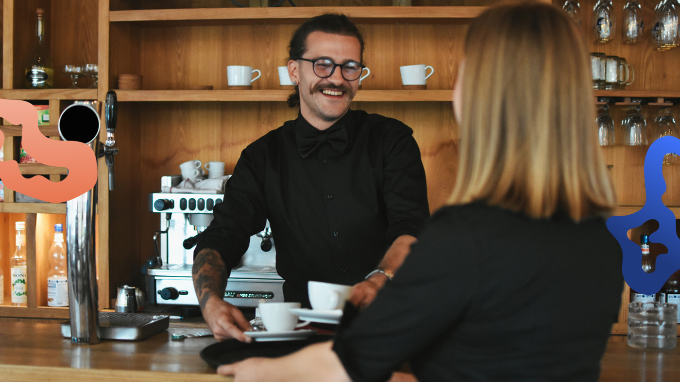 Glad kille som har ett deltidsjobb i Stockholm serverar kaffe till en gäst.